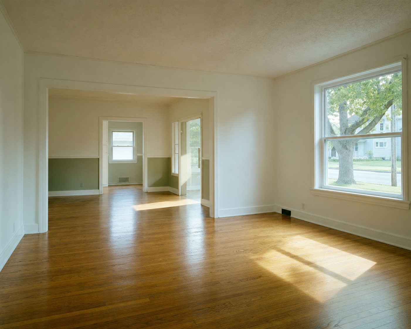 An empty, freshly cleaned sunlit room with polished hardwood floors